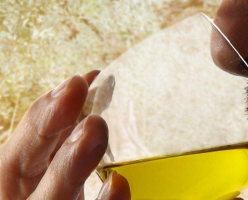 Uomo che esegue l’analisi sensoriale dell’olio extravergine di oliva, portando un bicchiere di vetro al naso per valutarne aroma e qualità.