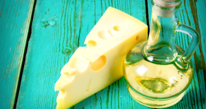Un pezzo di formaggio con buchi accanto a una bottiglia di olio su un tavolo in legno verde. Un'immagine che richiama l'abbinamento tra olio extravergine di oliva e formaggi.
