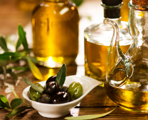 Bottiglie di olio extravergine di oliva accanto a un piattino con olive verdi e nere, su un tavolo in legno decorato con rami di ulivo, in un'atmosfera calda e rustica.