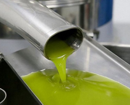 Flusso di olio extravergine di oliva verde brillante che esce da un tubo in acciaio inox durante la fase finale del processo di estrazione in un impianto oleario.