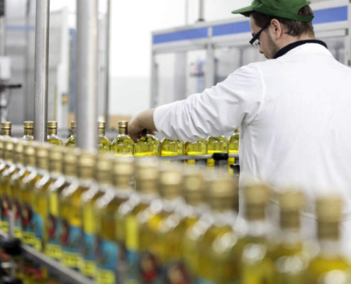 Operatore di linea controlla bottiglie di olio extravergine di oliva durante il processo di confezionamento industriale in uno stabilimento alimentare.