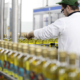Operatore di linea controlla bottiglie di olio extravergine di oliva durante il processo di confezionamento industriale in uno stabilimento alimentare.