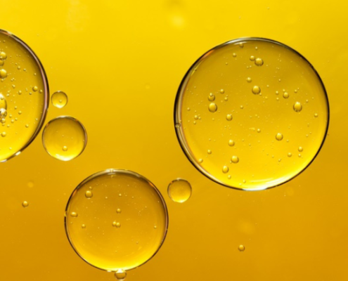 Macro di gocce di olio extravergine su sfondo giallo dorato, simbolo della purezza e dei polifenoli presenti nella varietà Coratina.
