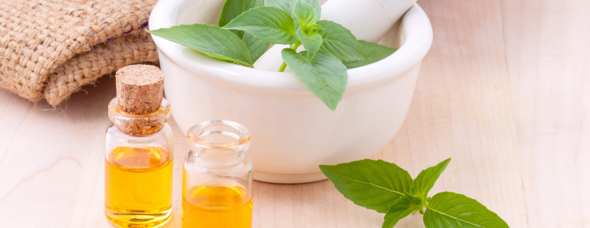 Foglie fresche di basilico in un mortaio con pestello e due boccette di olio aromatizzato, simbolo della preparazione dell’olio al basilico fatto in casa.