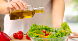 Persona che versa olio extravergine di oliva da una bottiglia su una ciotola di insalata fresca con lattuga, pomodorini e verdure colorate.