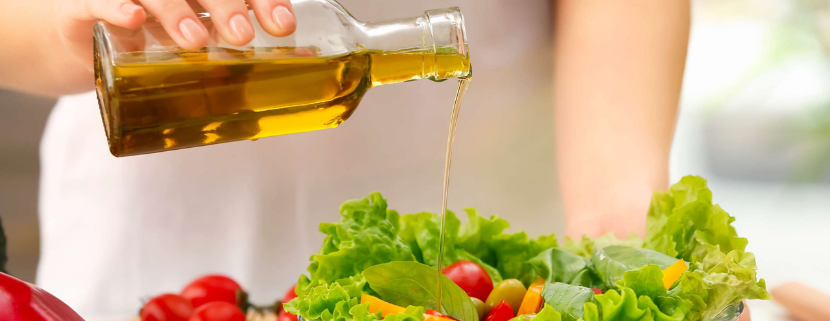 Persona che versa olio extravergine di oliva da una bottiglia su una ciotola di insalata fresca con lattuga, pomodorini e verdure colorate.