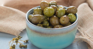 Ciotola in ceramica azzurra colma di olive verdi condite, appoggiata su un panno di juta, pronta per essere servita come antipasto o snack mediterraneo.