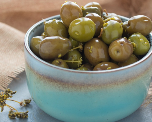Ciotola in ceramica azzurra colma di olive verdi condite, appoggiata su un panno di juta, pronta per essere servita come antipasto o snack mediterraneo.