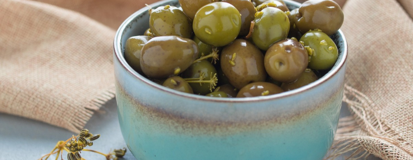 Ciotola in ceramica azzurra colma di olive verdi condite, appoggiata su un panno di juta, pronta per essere servita come antipasto o snack mediterraneo.