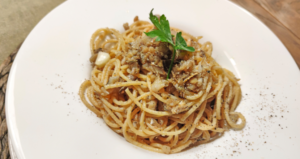 Piatto di spaghetti conditi con salsa di funghi e spezie, serviti in un piatto bianco e guarniti con una foglia di prezzemolo fresco.