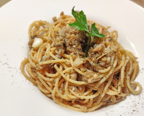 Piatto di spaghetti conditi con salsa di funghi e spezie, serviti in un piatto bianco e guarniti con una foglia di prezzemolo fresco.