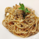 Piatto di spaghetti conditi con salsa di funghi e spezie, serviti in un piatto bianco e guarniti con una foglia di prezzemolo fresco.