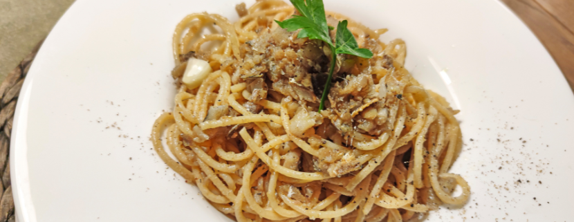 Piatto di spaghetti conditi con salsa di funghi e spezie, serviti in un piatto bianco e guarniti con una foglia di prezzemolo fresco.