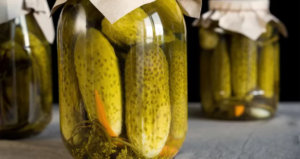 Cetriolini Sott'Olio: Guida Completa alla Ricetta, Conservazione e Abbinamenti Autentici Barattoli di vetro con cetrioli sott’aceto immersi in salamoia, chiusi con coperchi di carta, disposti su un piano di cucina in un ambiente rustico.
