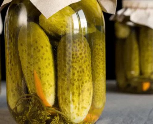 Barattoli di vetro con cetrioli sott’aceto immersi in salamoia, chiusi con coperchi di carta, disposti su un piano di cucina in un ambiente rustico.