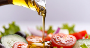 Olio di Oliva a Digiuno: Controindicazioni, Benefici e Consigli per una Scelta Consapevole Olio d’oliva versato su un’insalata fresca composta da pomodori, cetrioli e verdure.