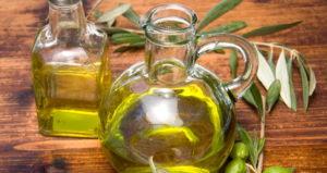 Quanto Olio al Giorno? Guida Completa a Benefici, Dosi Consigliate e Consumo Consapevole Bottiglie di vetro trasparente piene di olio extravergine di oliva su tavolo di legno, decorate con rami e frutti di ulivo freschi.