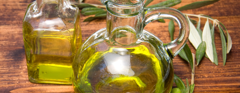 Bottiglie di vetro trasparente piene di olio extravergine di oliva su tavolo di legno, decorate con rami e frutti di ulivo freschi.