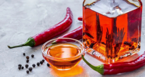 Olio Piccante Come Farlo: Guida Completa a Ricetta, Varianti e Consigli per un Olio Aromatizzato Autentico Bottiglia e ciotolina di olio piccante con peperoncini rossi e grani di pepe, preparazione artigianale di olio aromatizzato al peperoncino.