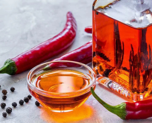 Bottiglia e ciotolina di olio piccante con peperoncini rossi e grani di pepe, preparazione artigianale di olio aromatizzato al peperoncino.