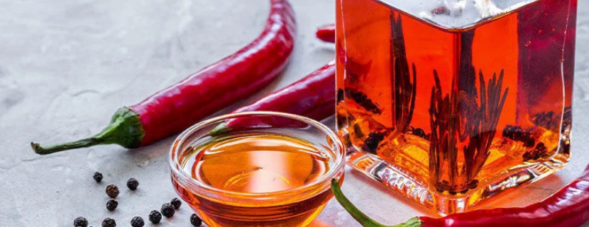 Bottiglia e ciotolina di olio piccante con peperoncini rossi e grani di pepe, preparazione artigianale di olio aromatizzato al peperoncino.